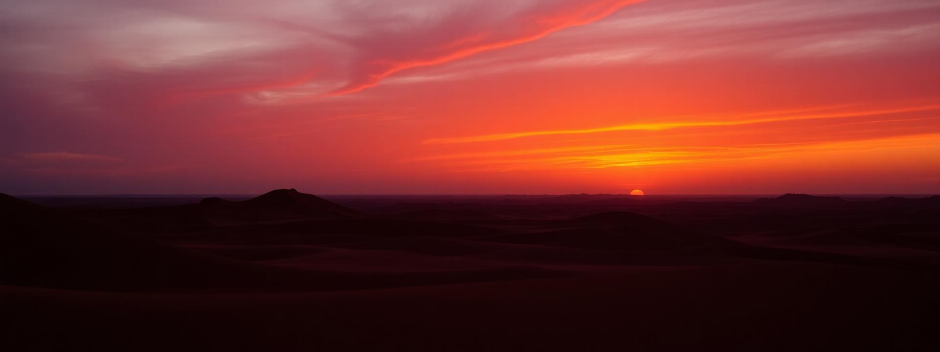 Wide desert horizon at sunset with red dune silhouettes